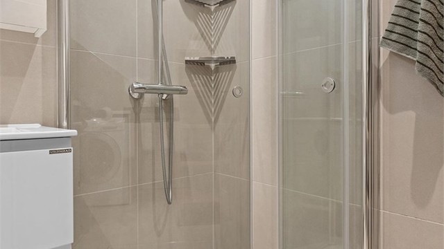 Badet har flislagte overflater, gulvvarme og et praktisk dusjhjørne med glassdører.