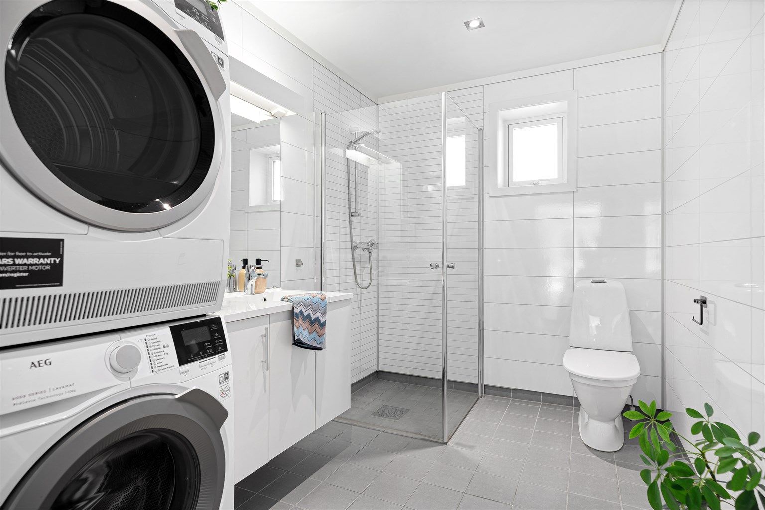 Tidløst og innholdsrikt bad med fliser på gulv og gulvvarme samt baderomsplater på vegg. Videre er det dusnisje med innfellbare dører og toalett. 