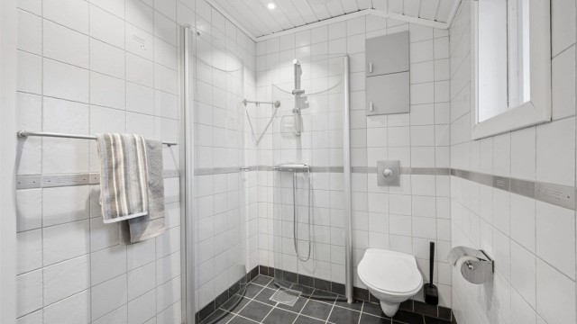 Dusjhjørne med buet innfellbare glassdører og dusjarmatur tilkoblet veggmontert hånddusj.