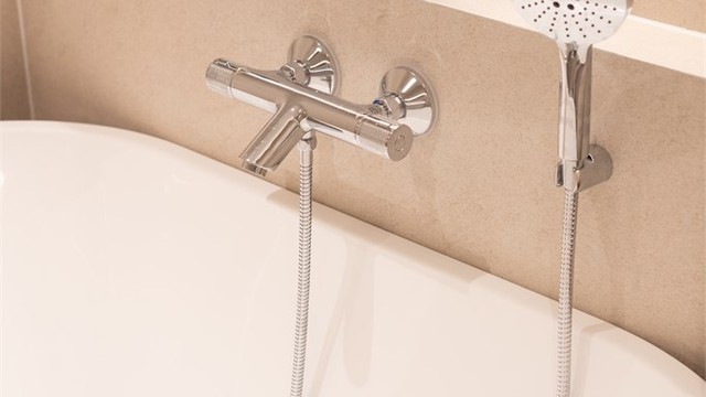 Badekar med moderne kombinert bade-/dusjbatteri og veggmontert hånddusj.
