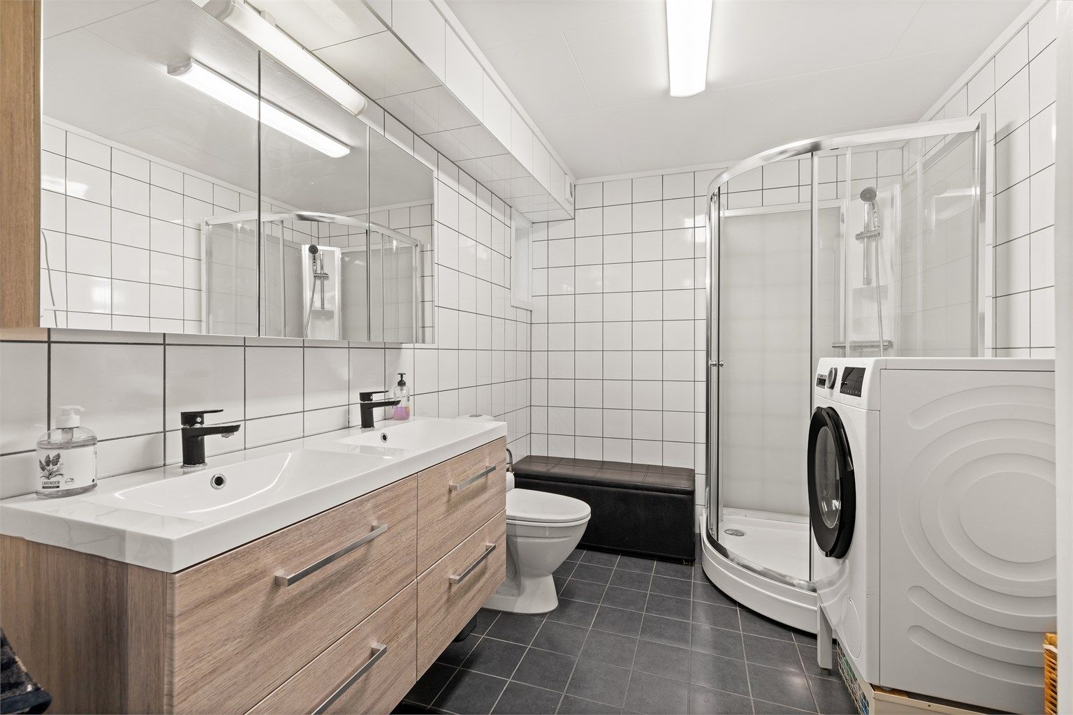 Gulvmontert toalett og dusjkabinett med glassdører. Mekanisk avtrekksvifte i vegg. Innredning og kabinett fra 2021.