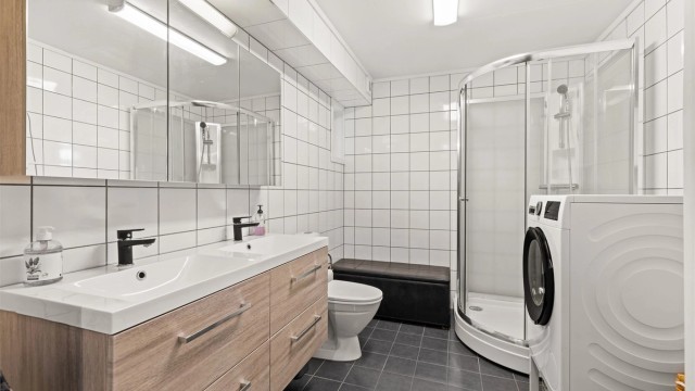 Gulvmontert toalett og dusjkabinett med glassdører. Mekanisk avtrekksvifte i vegg. Innredning og kabinett fra 2021.