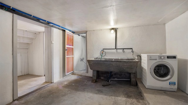 Separat vaskerom med gulvstående utslagsvask og vaskemaskin i kjeller