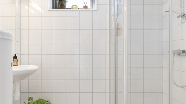 Baderom fra byggeår. Flislagt gulv med gulvvarme. Flislagte vegger. Takplater i himling. Vegghengt servantinnredning. Speil med overlys. Dusjhjørne med dører. Gulvstående toalett.