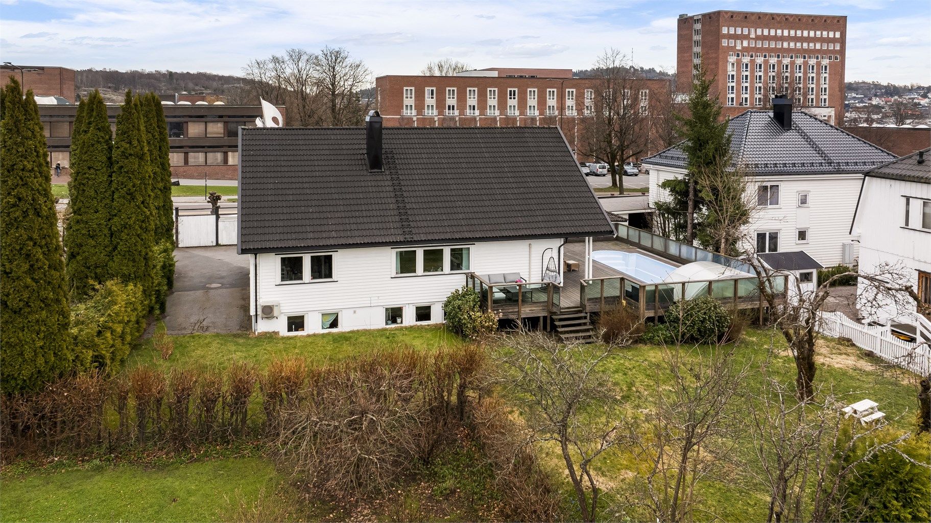 Eiendommen sett fra hagesiden, med terrassen og bassenget sentralt plassert.