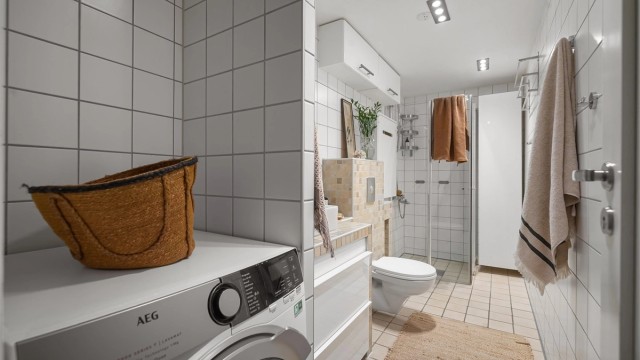 Innbydende og meget romslig bad med hvite fliser på vegg, beigemelerte fliser på gulv med varmekabler og downlights i himling