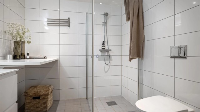 Badet er utstyrt med vegghengt toalett og dusjhjørne med innfellbare glassdører