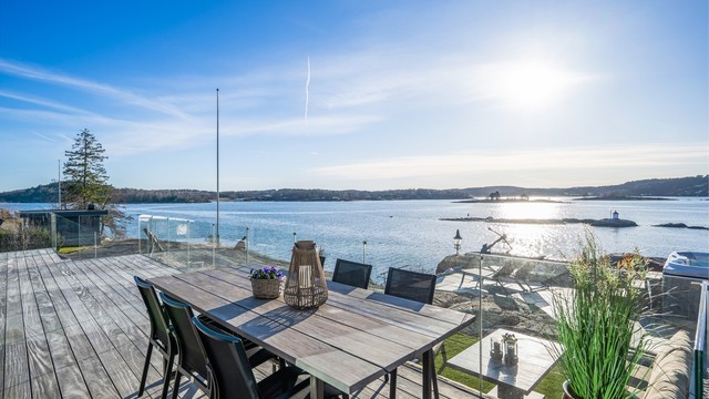 Utgang fra stue og spisestue i 1. etasje via store skyvedører til vestvendt terrasse oppført med vedlikeholdsvennlig tredekke og rekkverk i glass.