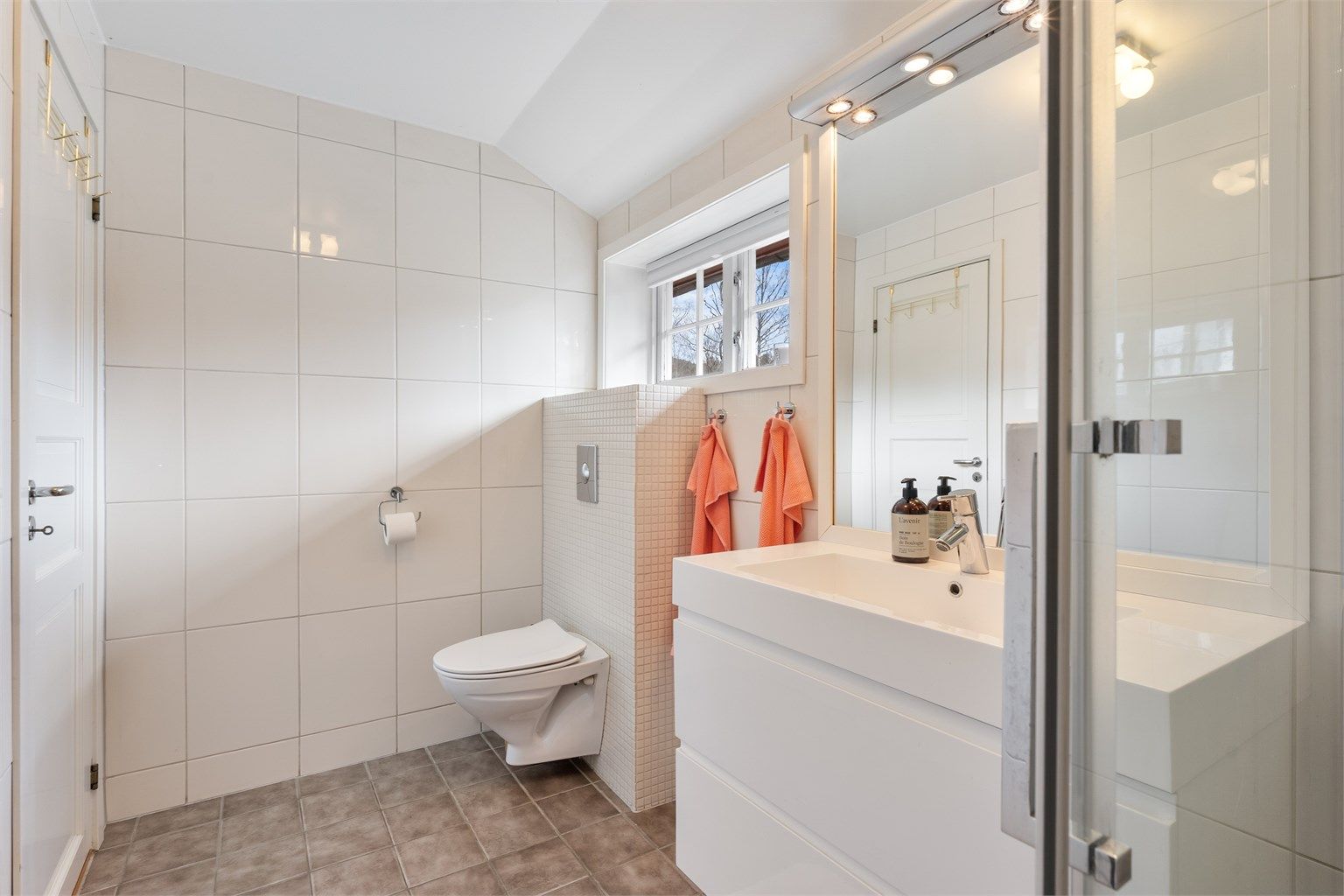 Badet er utstyrt med vegghengt toalett, innredning med skuffer og dusjløsning med regnfallsdusj.