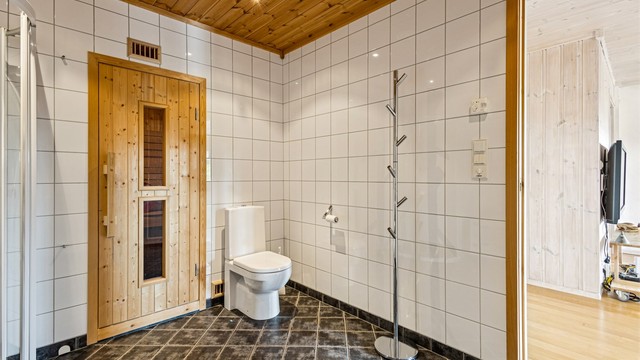 Romslig baderom med fliser på vegger og gulv samt panelbord i himlingen.