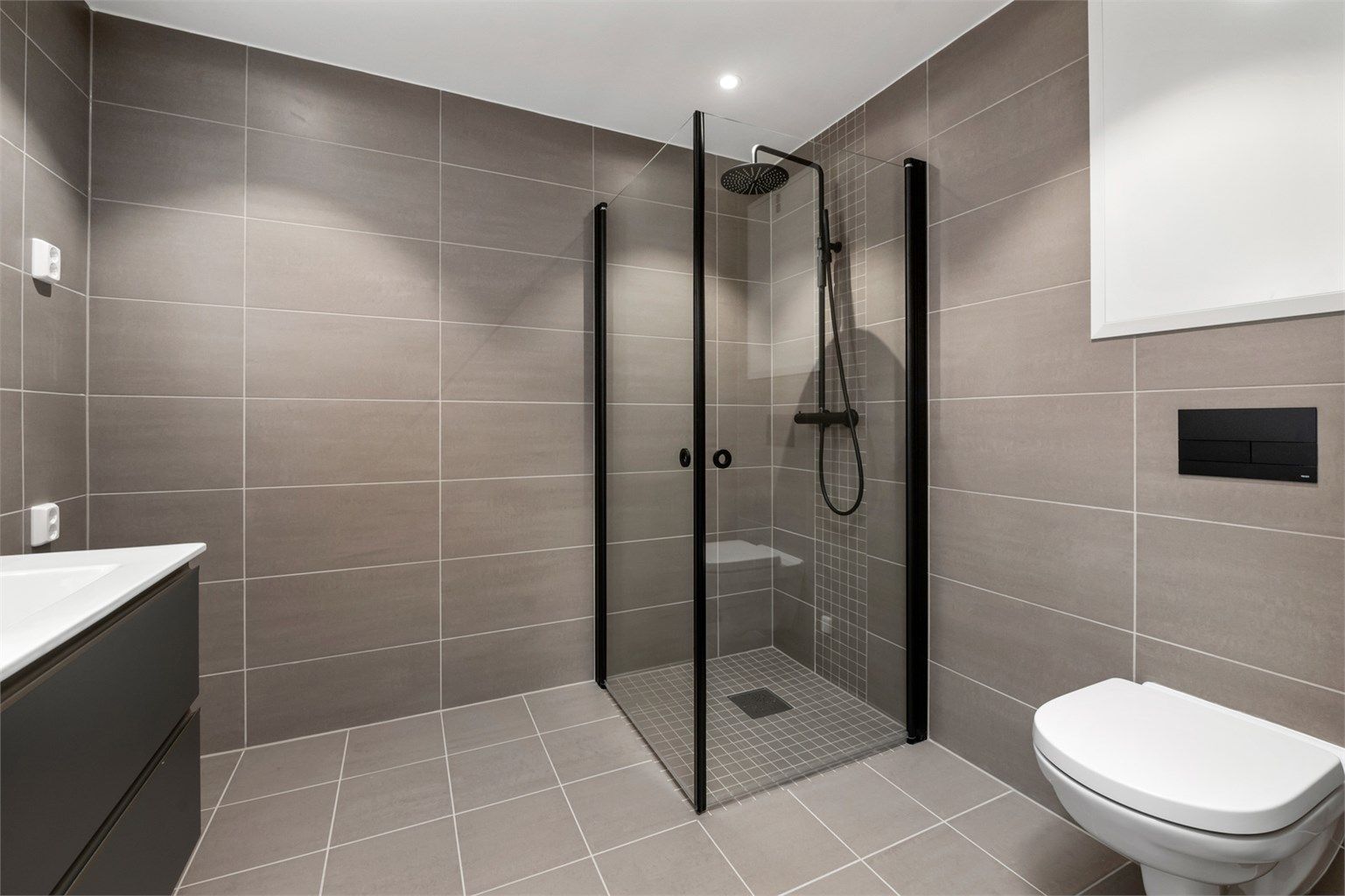 Badet inneholder servantskap, speil med innebygd lys, vegghengt toalett og dusjhjørne med innfellbare vegger.