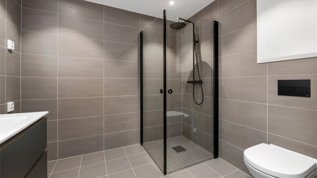 Badet inneholder servantskap, speil med innebygd lys, vegghengt toalett og dusjhjørne med innfellbare vegger.