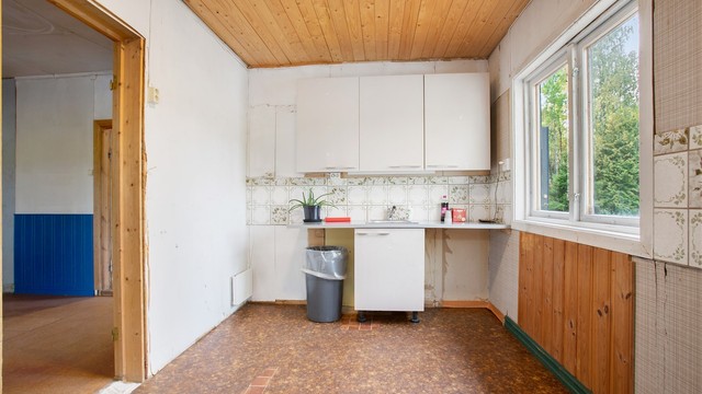 Kjøkkeninnredning med glatte fronter, laminert benkeplate og vindu mot tunet.