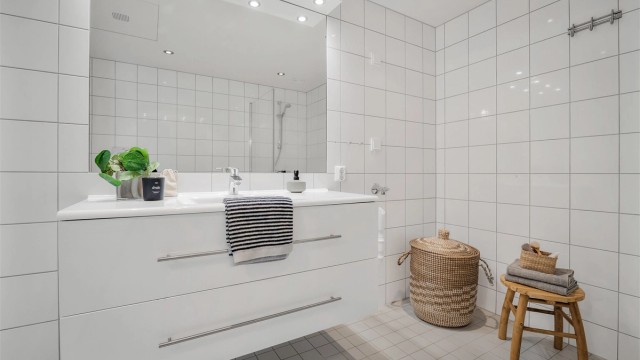 Badet har dusjhjørne med foldedører av glass og opplegg for vaskemaskin.