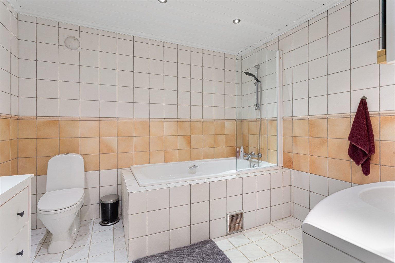 Flislagt bad med downlights i taket og dusjløsning i badekaret.