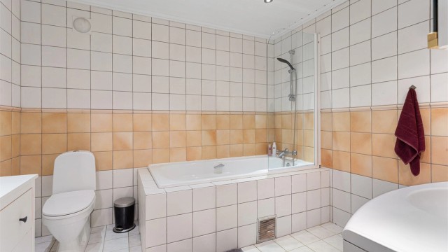 Flislagt bad med downlights i taket og dusjløsning i badekaret.