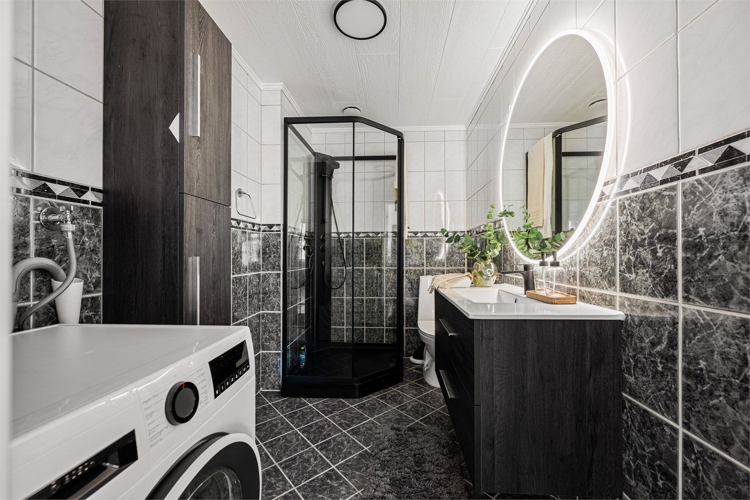 Romslig helfliset bad av godt med varme i gulv. Det er mørke fliser på gulv og delvis på vegg ,ellers lyse fliser. På bad er det ellers toalett og ekstra skap på vegg til oppbevaring.  Opplegg for vaskemaskin samt plass til tørketrommel.