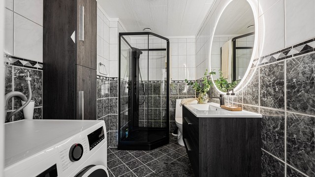 Romslig helfliset bad av godt med varme i gulv. Det er mørke fliser på gulv og delvis på vegg ,ellers lyse fliser. På bad er det ellers toalett og ekstra skap på vegg til oppbevaring. Opplegg for vaskemaskin samt plass til tørketrommel.