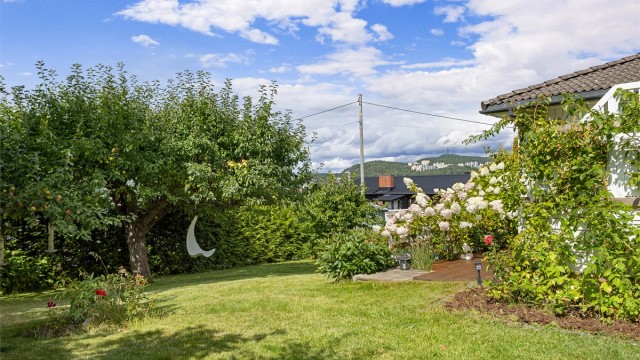 Den pent opparbeidede hagen byr på plen, frukttrær og variert beplantning og gir en grønn og trivelig ramme rundt boligen.