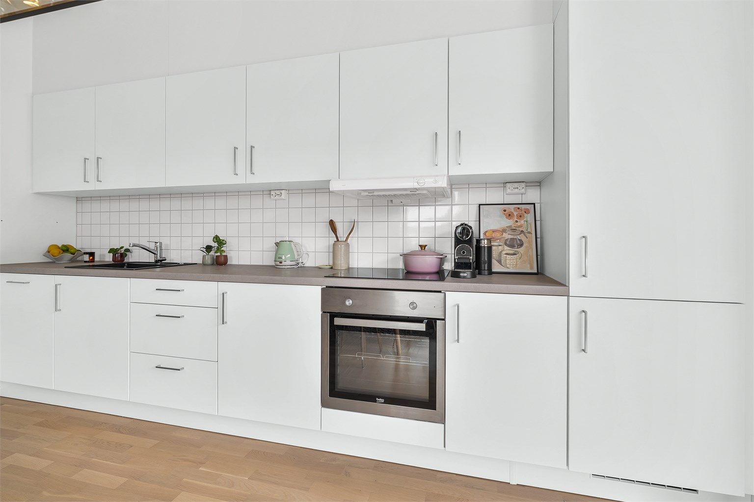 Kjøkkeninnredning med glatte fronter og integrerte hvitevarer som stekeovn, induksjonstopp, oppvaskmaskin og kjøl/fryseskap.