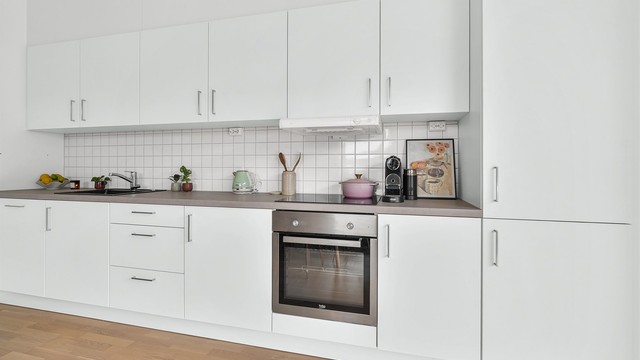 Kjøkkeninnredning med glatte fronter og integrerte hvitevarer som stekeovn, induksjonstopp, oppvaskmaskin og kjøl/fryseskap.