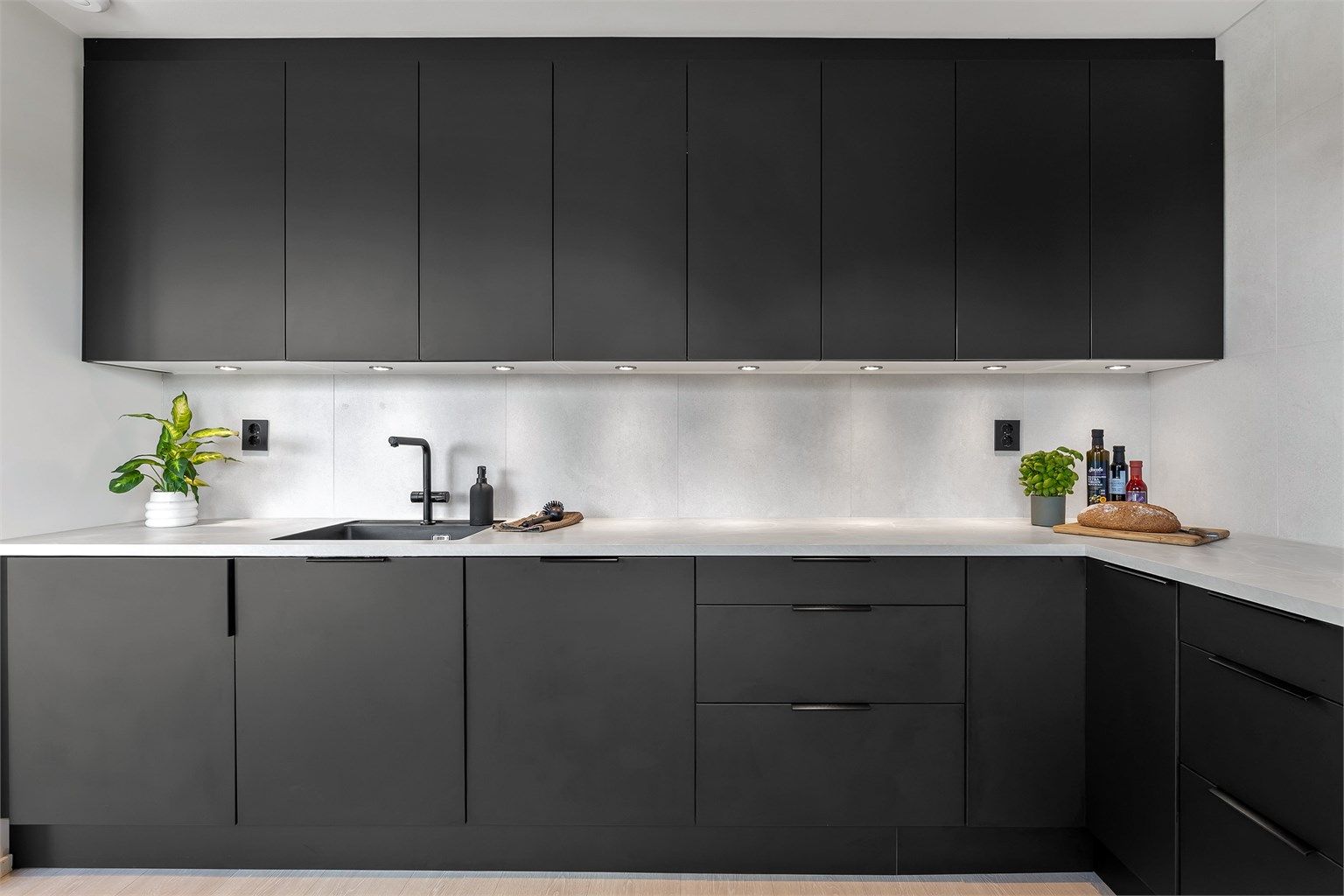 Designa kjøkken fra 2022 med glatte fronter, kjøkkenøy og benkeplate med laminert overflate. Nedfelt kjøkkenvask med armatur. Belysning under benkeskap og stikkontakter over kjøkkenbenk.