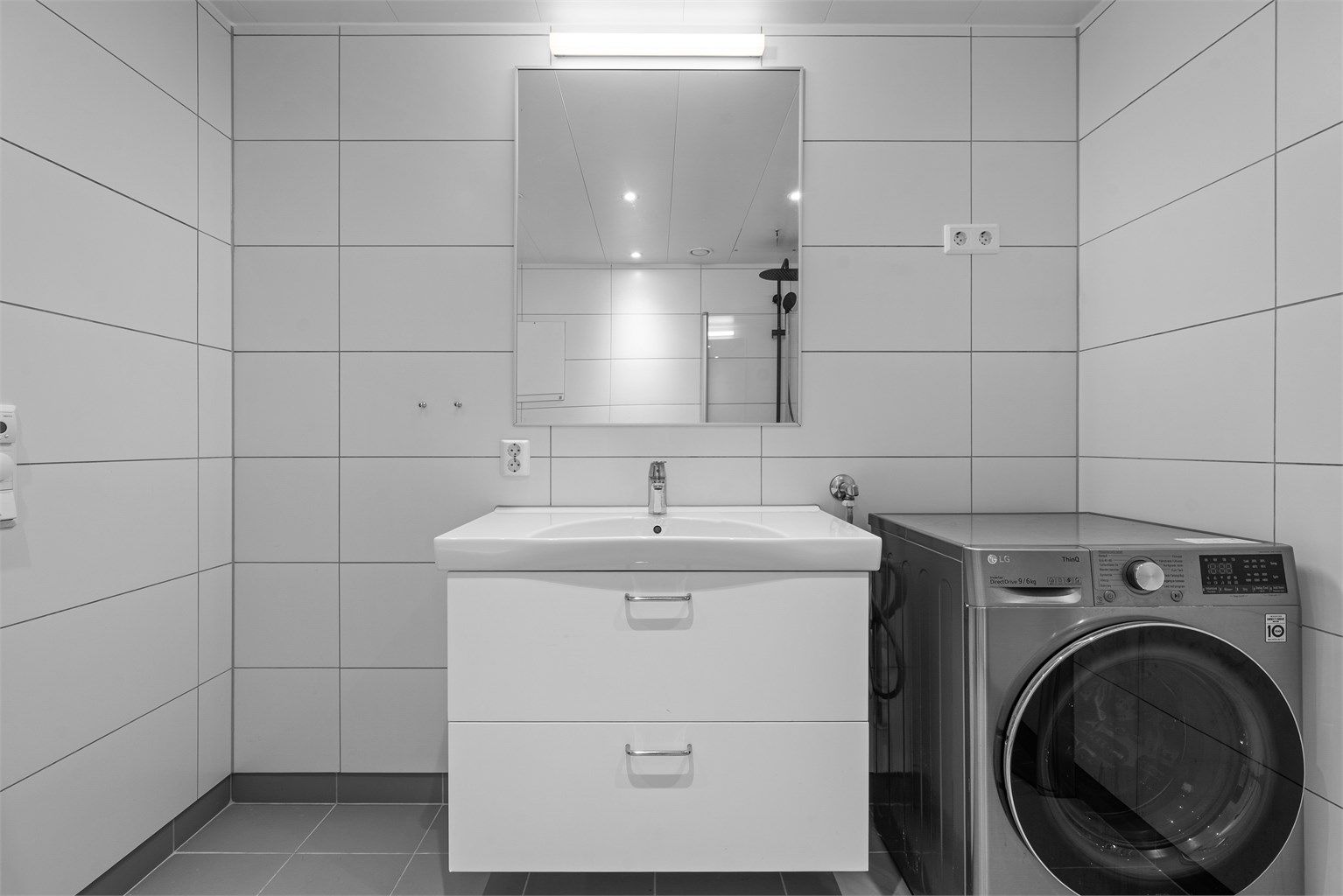 Badet har opplegg for vaskemaskin og en stilren servantinnredning med skuffer.
