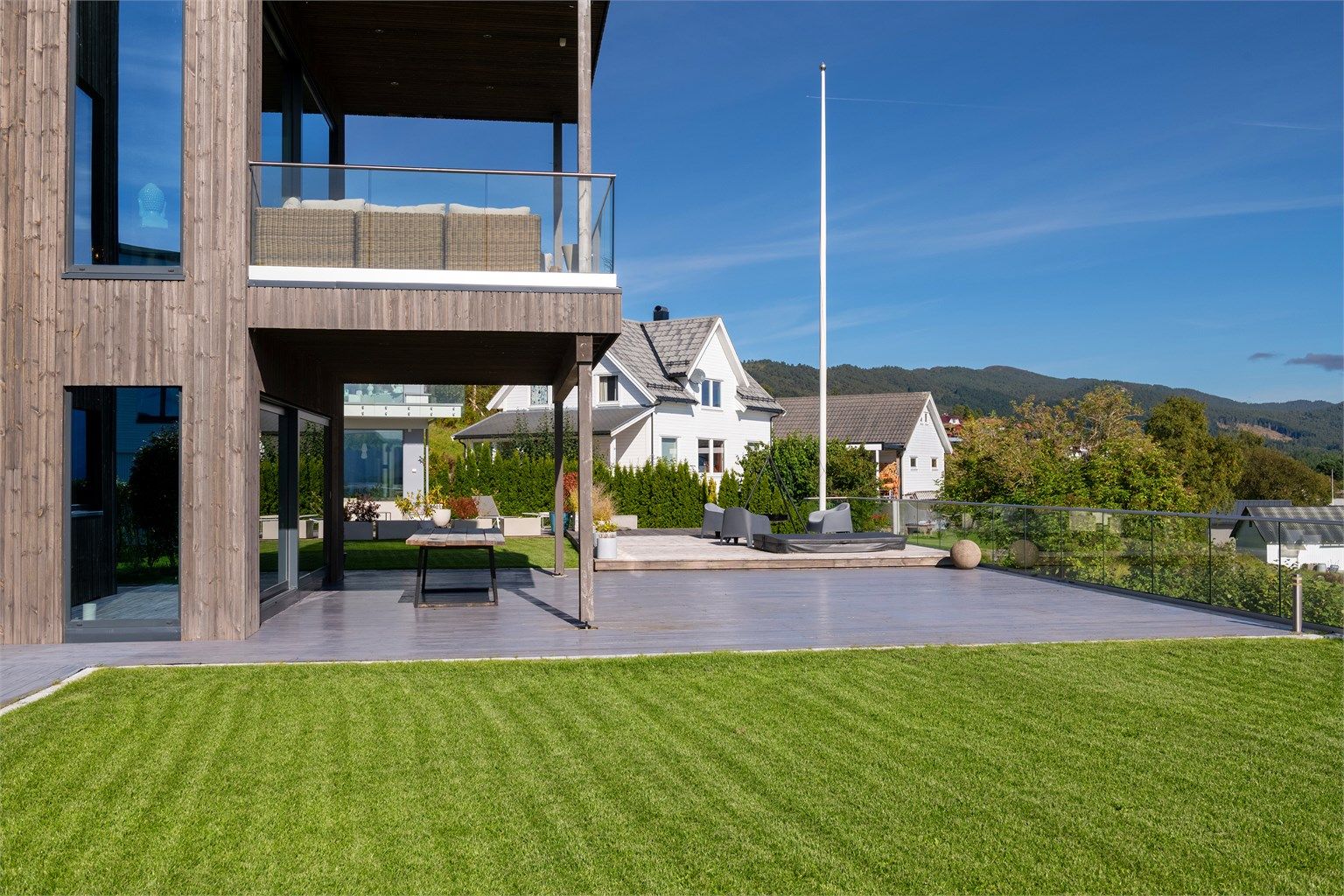 Eiendommen har en flat, terrassert tomt med gressplen og glassrekkverk i ytterkant.