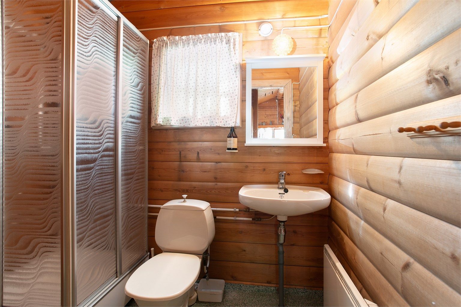 Badet er innredet med dusjkabinett, servant, toalett og panelovn.