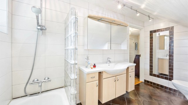 Flislagte vegger og vegghengt toalett på badet i loftsetasjen.