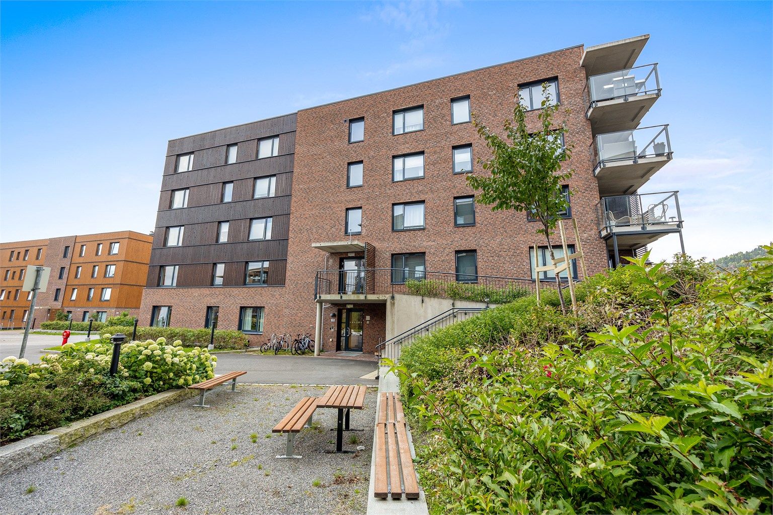 Opparbeidet fellesareal med sittegrupper, beplantning og asfalterte gangveier.