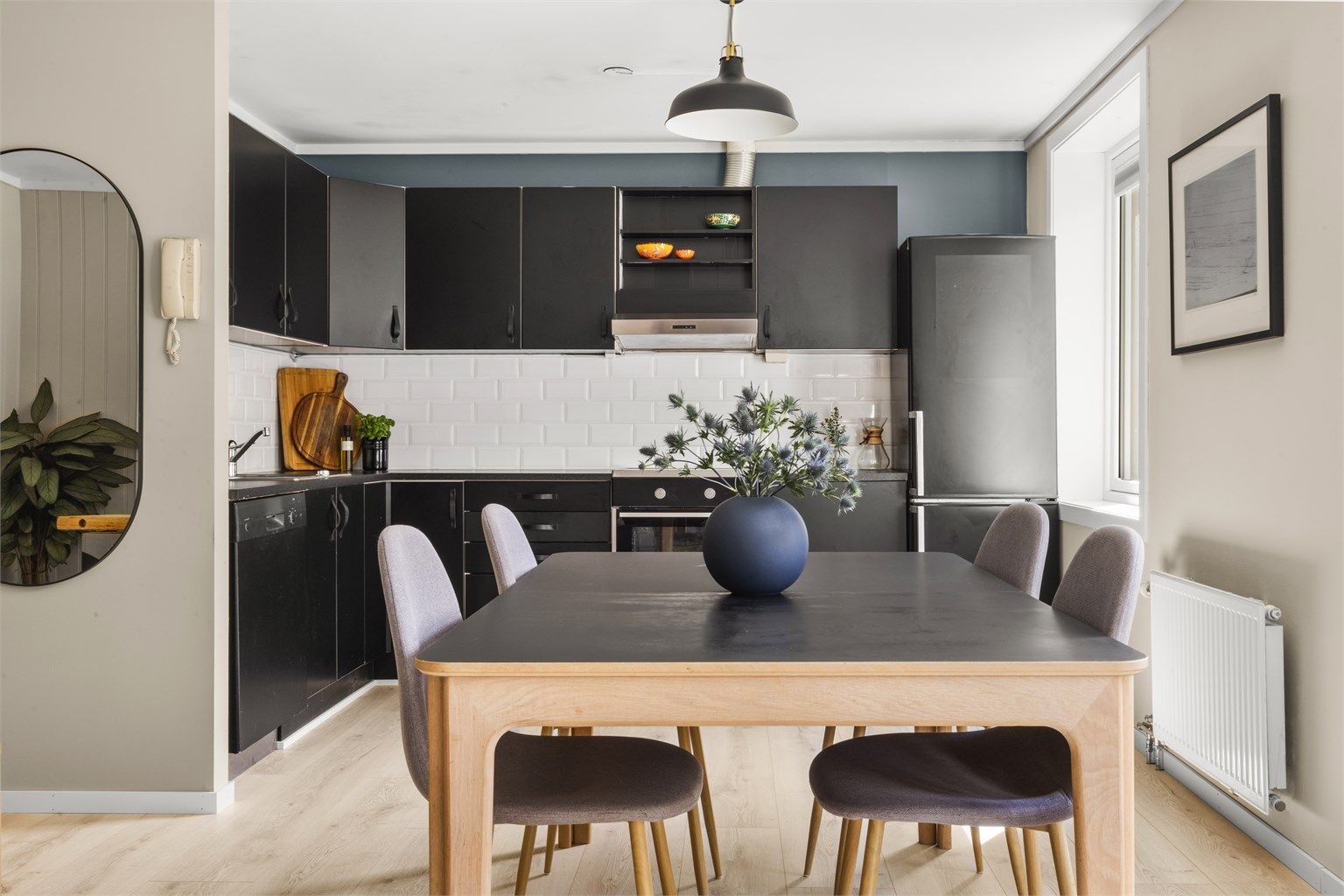 Stilren og moderne kjøkkenløsning med svarte fronter, lyse gulv og god spiseplass i naturlig lys fra store vindusflater.