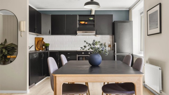 Stilren og moderne kjøkkenløsning med svarte fronter, lyse gulv og god spiseplass i naturlig lys fra store vindusflater.