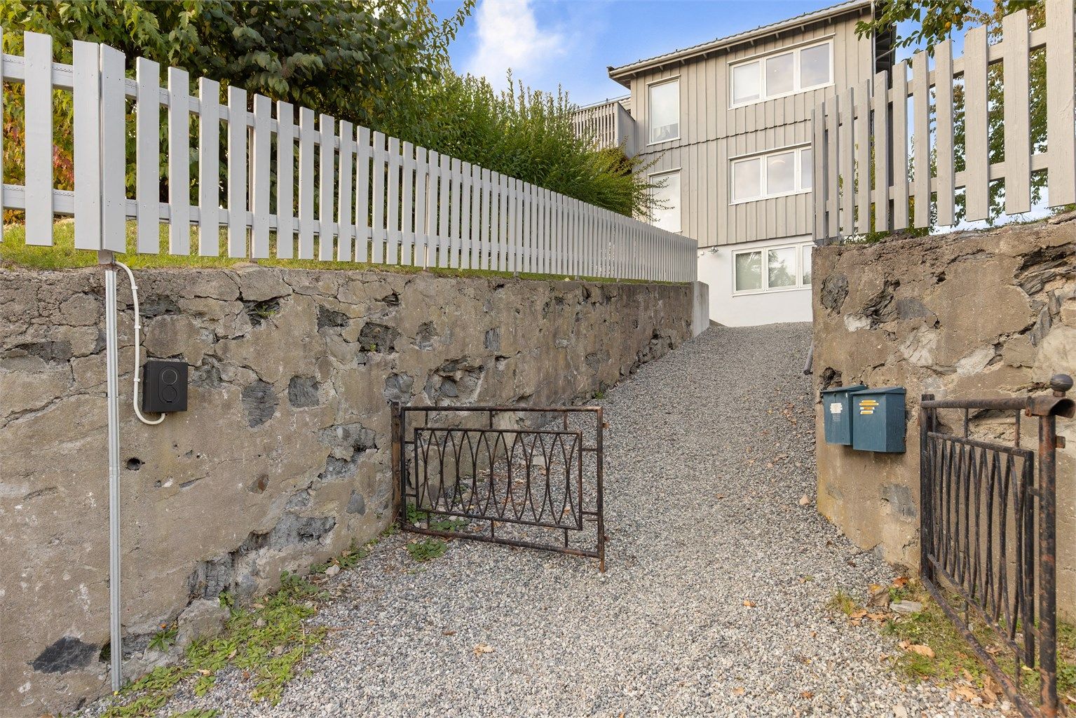 Gruslagt innkjøring med forstøtningsmur i naturstein og montert lader for elbil.