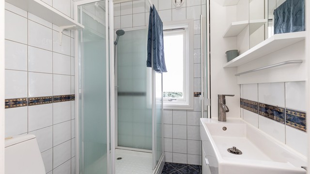 Badet har flislagte vegger og gulv, utstyrt med dusjkabinett og vindu for naturlig dagslys.
