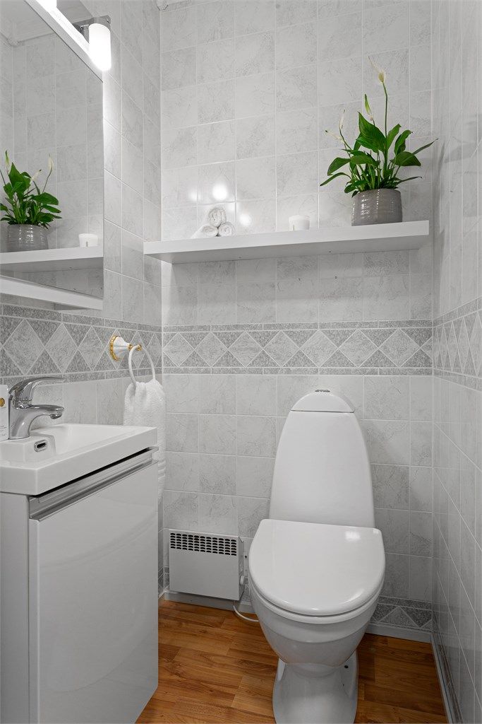 Toalettrom med laminat på gulv og veggflater med våtromsplater. Innredet med vegghengt servantskap med slett dør og ovenpåliggende servant. Speilskap og lys på vegg over servant. Gulvstående toalett og oppvarming med panelovn