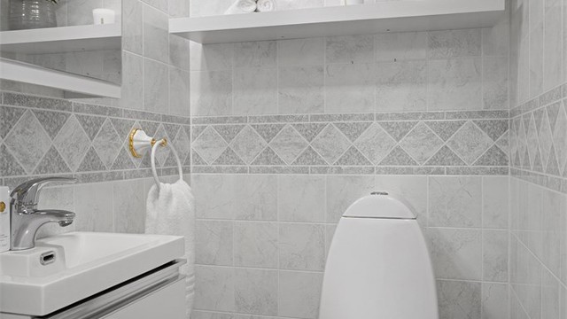 Toalettrom med laminat på gulv og veggflater med våtromsplater. Innredet med vegghengt servantskap med slett dør og ovenpåliggende servant. Speilskap og lys på vegg over servant. Gulvstående toalett og oppvarming med panelovn