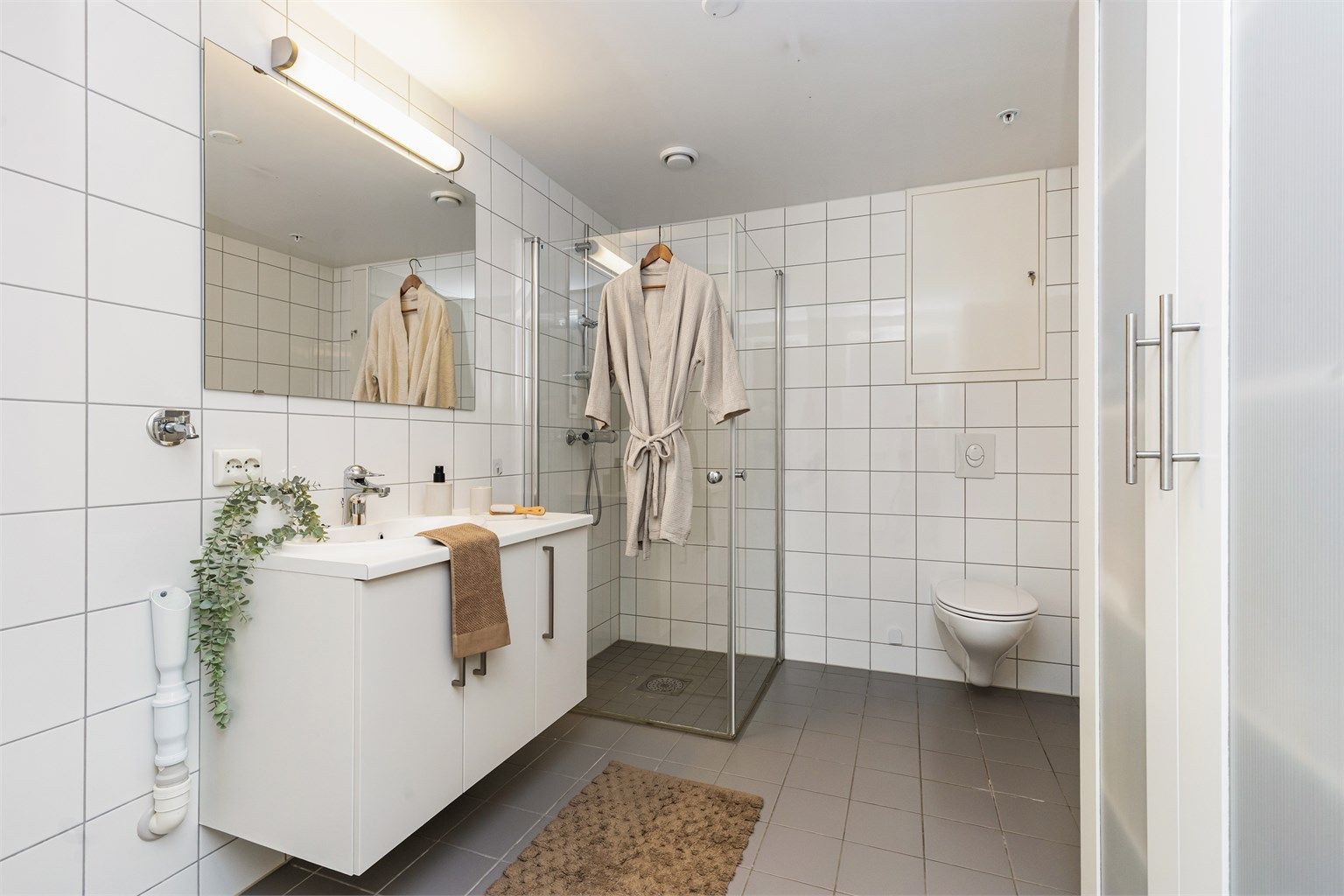 Helfliset bad med gulvvarme, vegghengt toalett, dusjhjørne med glassdører og opplegg for vaskemaskin.