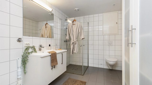 Helfliset bad med gulvvarme, vegghengt toalett, dusjhjørne med glassdører og opplegg for vaskemaskin.