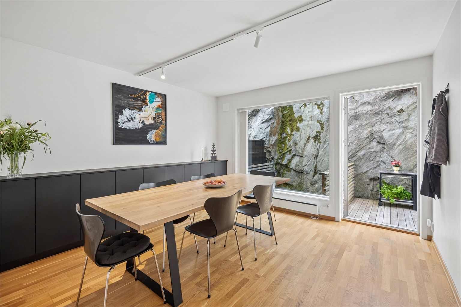 Spisestuen har store vindusflater mot hagen som gir en sømløs forbindelse mellom inne- og uterommet. Naturen bringes inn og skaper en atmosfære av ro og åpenhet.