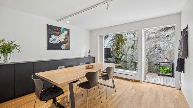 Spisestuen har store vindusflater mot hagen som gir en sømløs forbindelse mellom inne- og uterommet. Naturen bringes inn og skaper en atmosfære av ro og åpenhet.