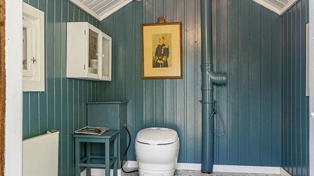 Pen utedo med tradisjonelt preg, oppusset med panelvegger i mørk blåtone og flismønstret gulvbelegg.