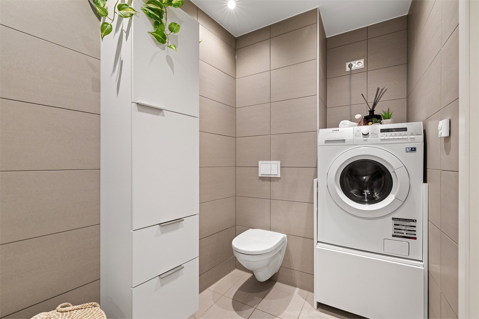 Badet har vegghengt toalett, dusjhjørne med innfellbare glassdører og opplegg for vaskemaskin.