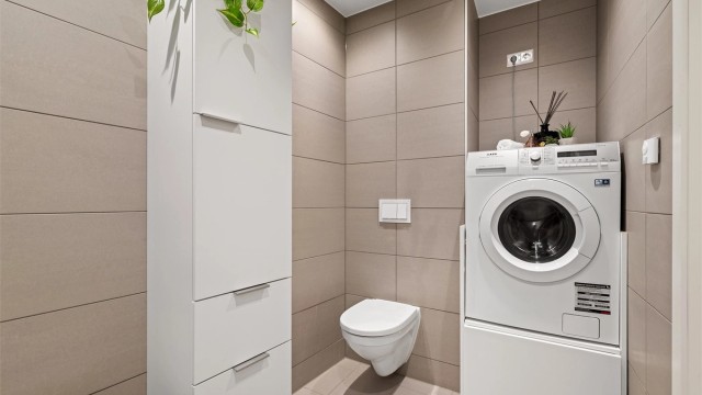 Badet har vegghengt toalett, dusjhjørne med innfellbare glassdører og opplegg for vaskemaskin.