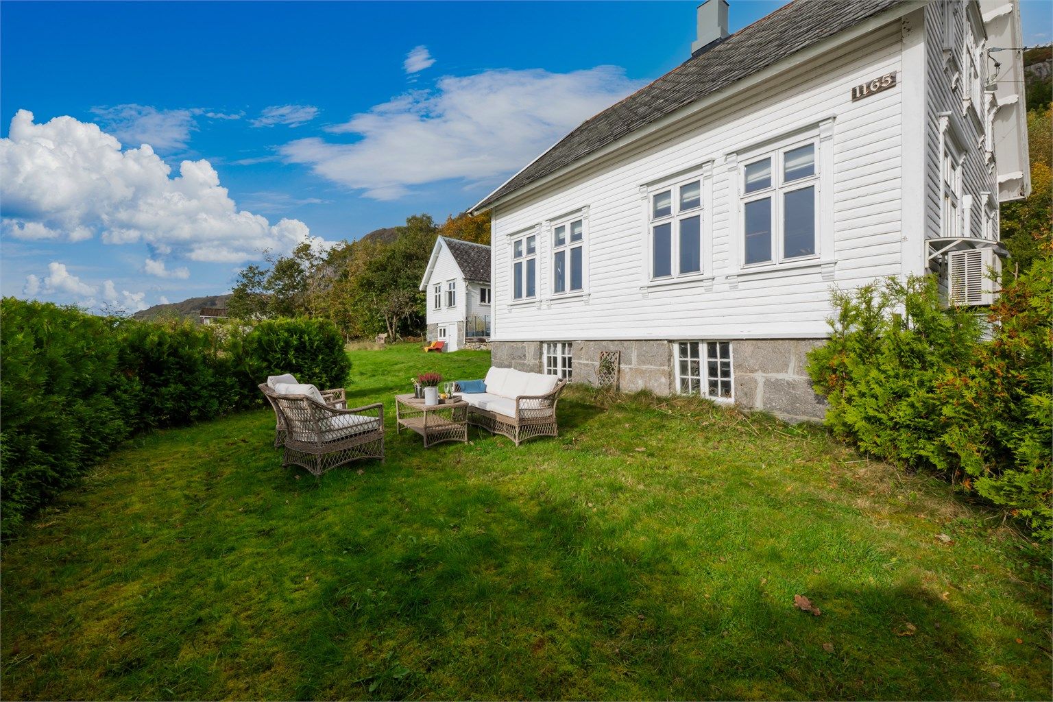 Romslig hageareal med gressplen og sitteplass på nedsiden av boligen.