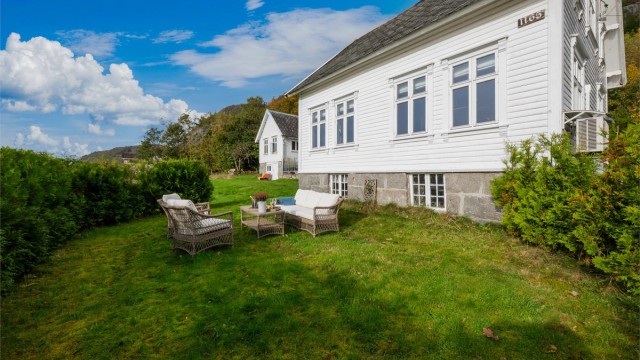 Romslig hageareal med gressplen og sitteplass på nedsiden av boligen.