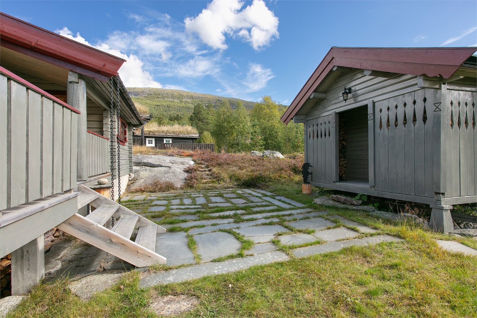 Skiferlagt uteplass mellom hovedhytta og annekset i naturlig fjellterreng.