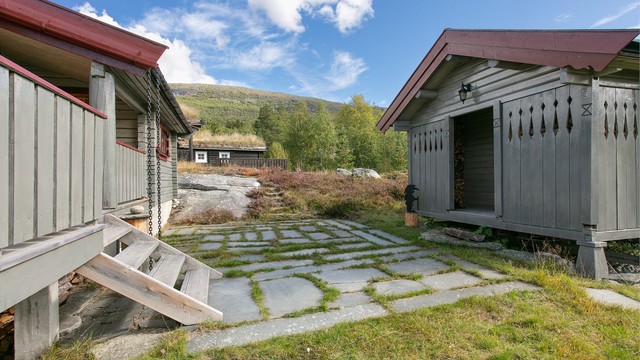 Skiferlagt uteplass mellom hovedhytta og annekset i naturlig fjellterreng.