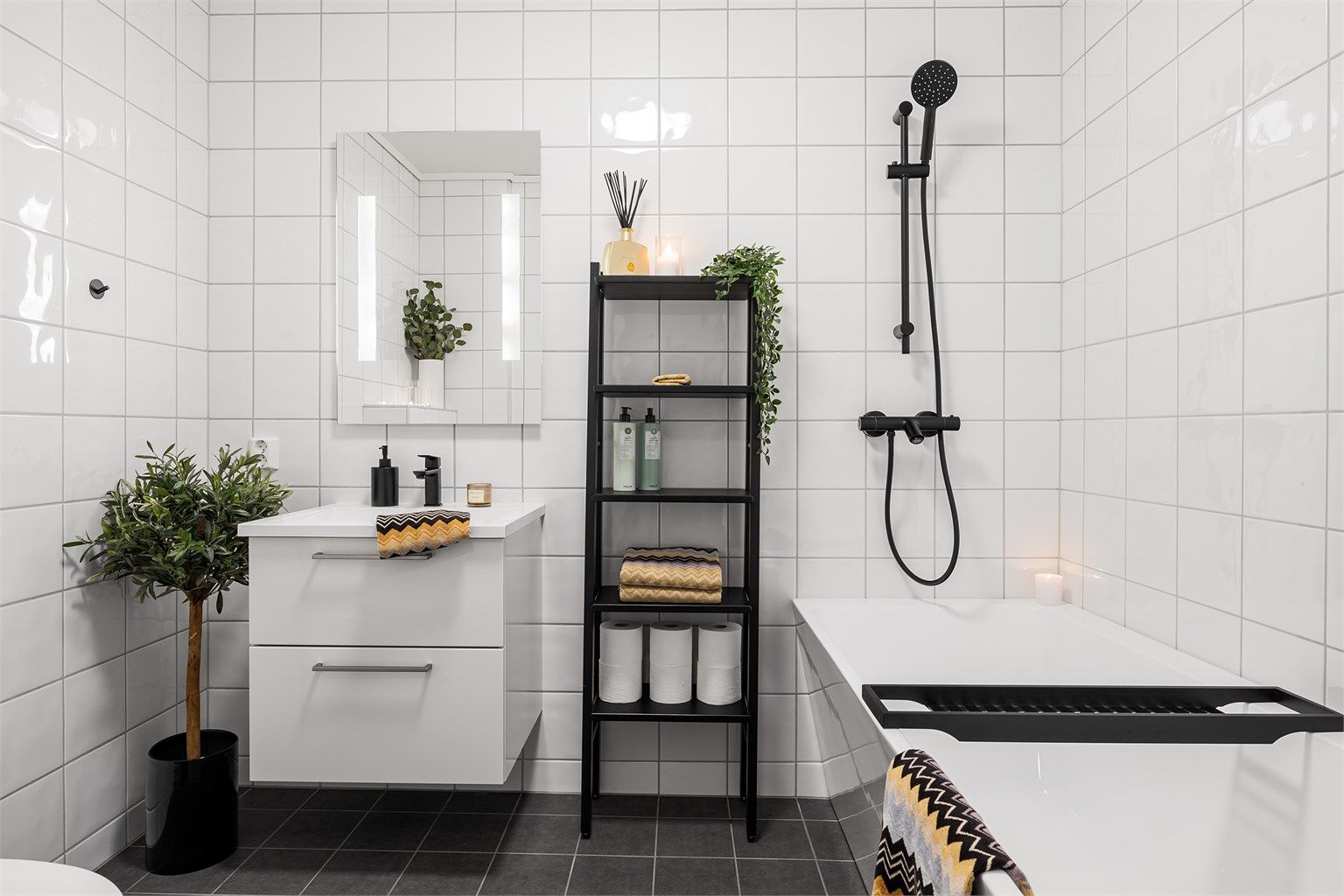 Flott flislagt bad i hovedetasjen med badekar med vegghengt dusjarmatur. Innredning med skuffer og speil med sidelys over servant. Vegghengt toalett