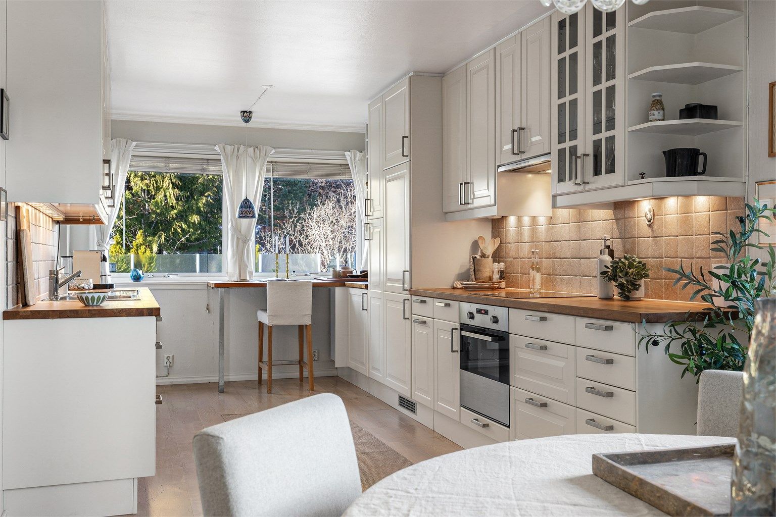 Kjøkken med innredning fra rundt 2010. Profilerte fronter. Benkeplate av tre. Nedfelt kjøkkenvask med armatur. Benkeskapsbelysning og stikkontakter over kjøkkenbenk.